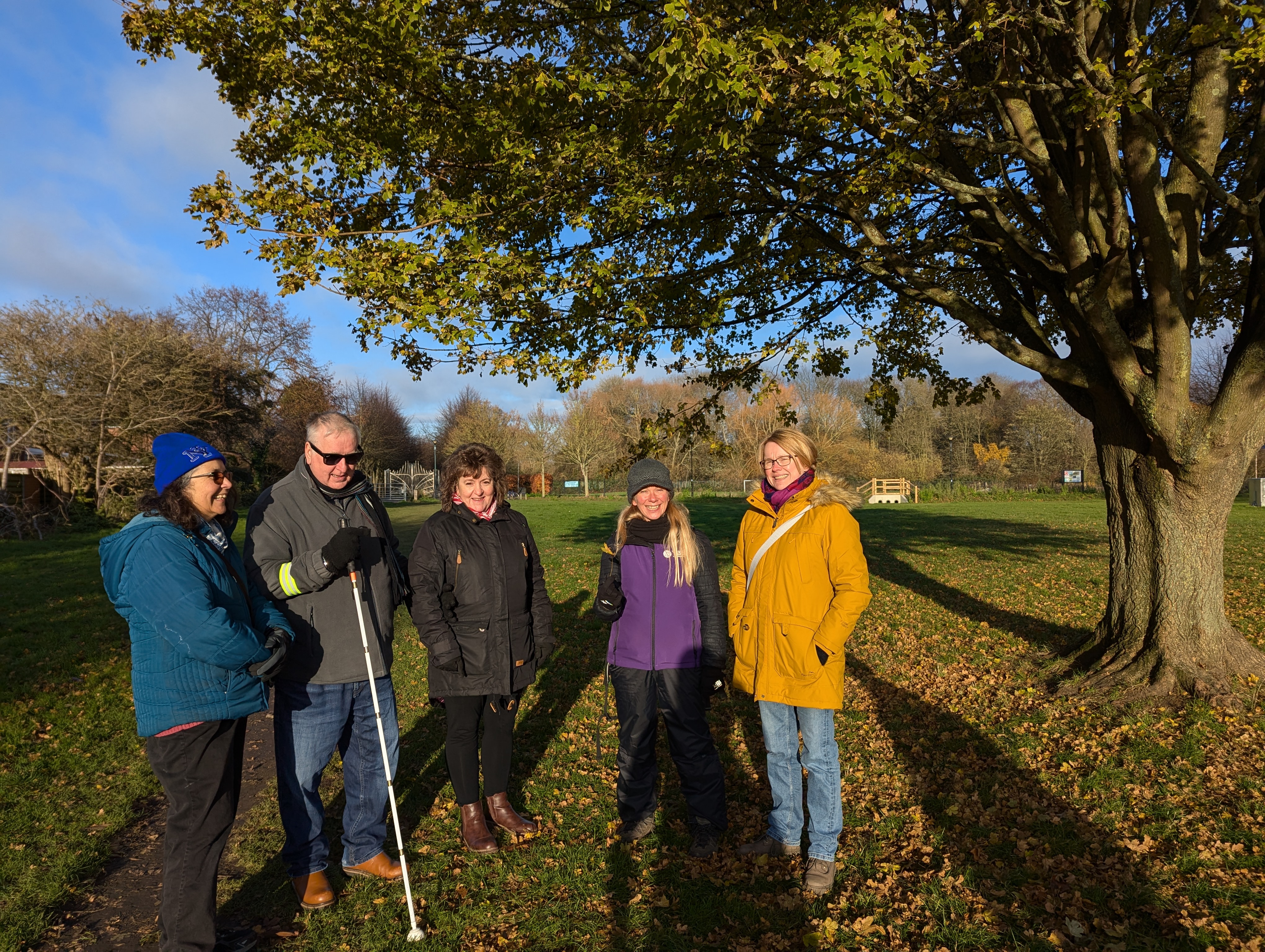 Group of people stand under a tree in the sunshine