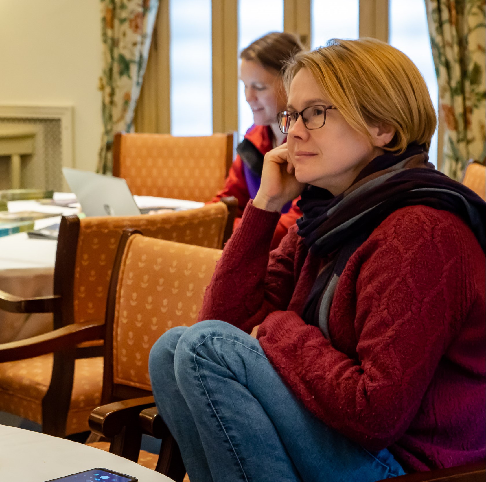 Woman sits with knees up on chair, listening intently
