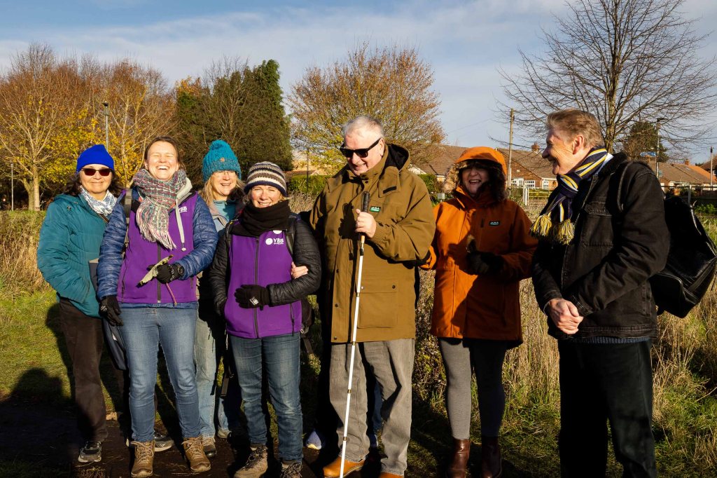 Group stand together in t sunshine, smiling.