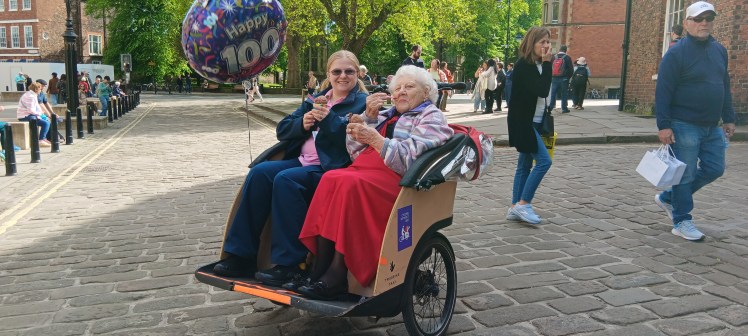 Two women, one with 100 balloon eat ice cream on the Triobike