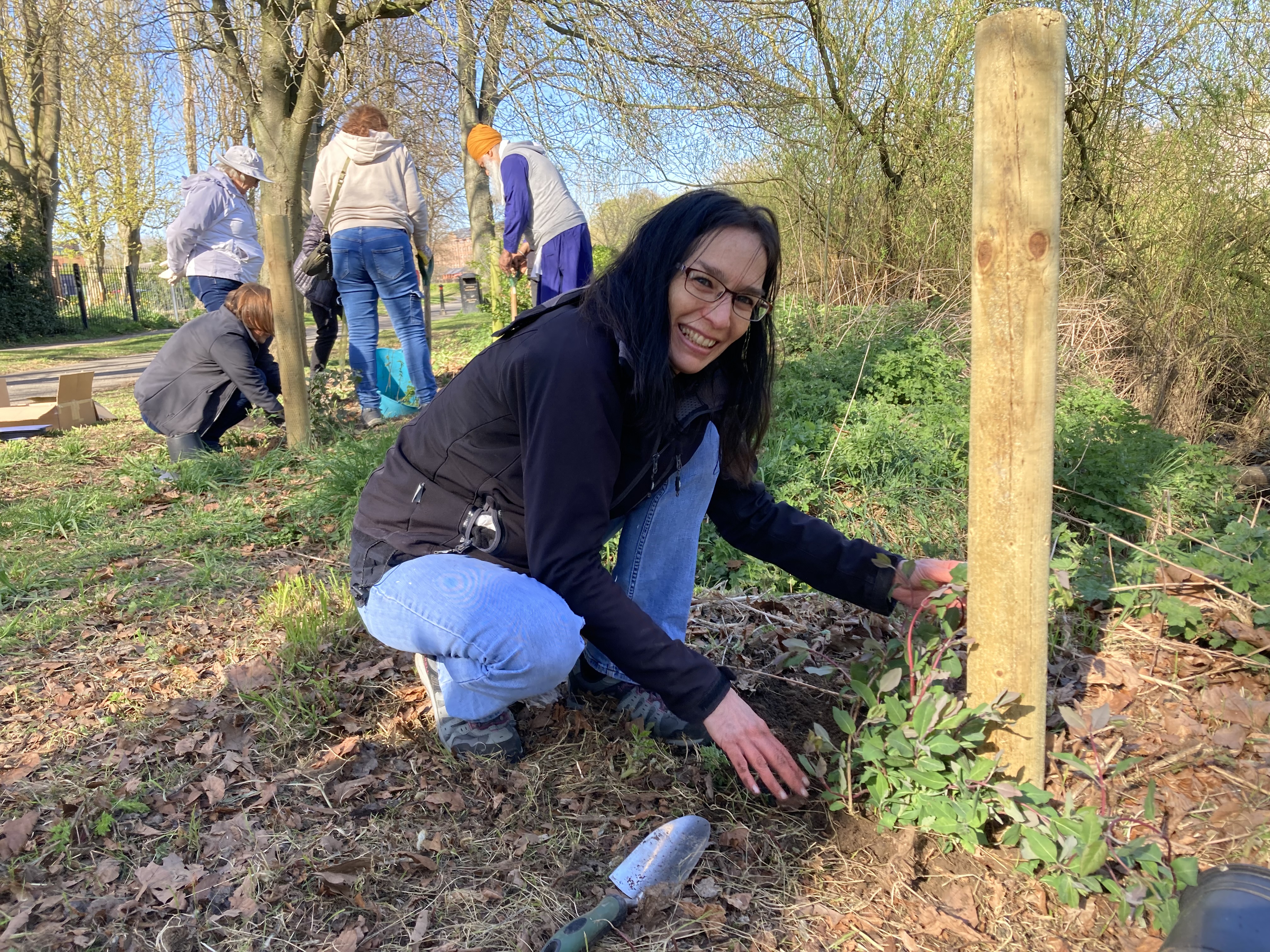 Woman smiling as she plants Honeysuckle plant, people working behind.