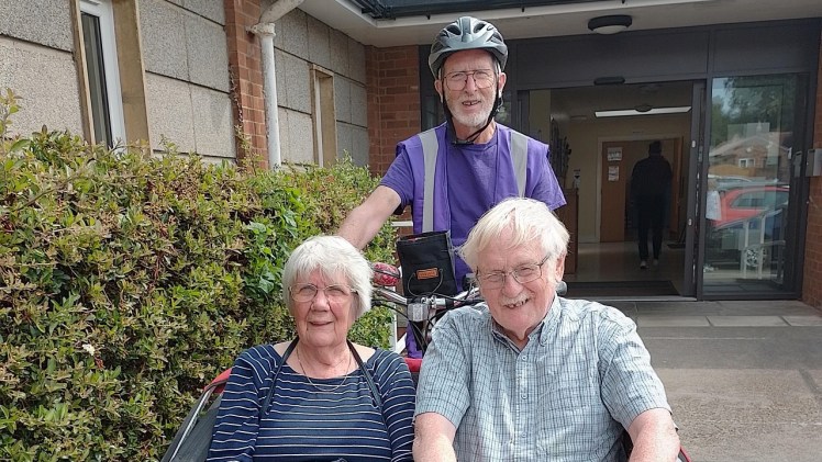 A man in a purple vest pedalling a Trixie bike with passengers