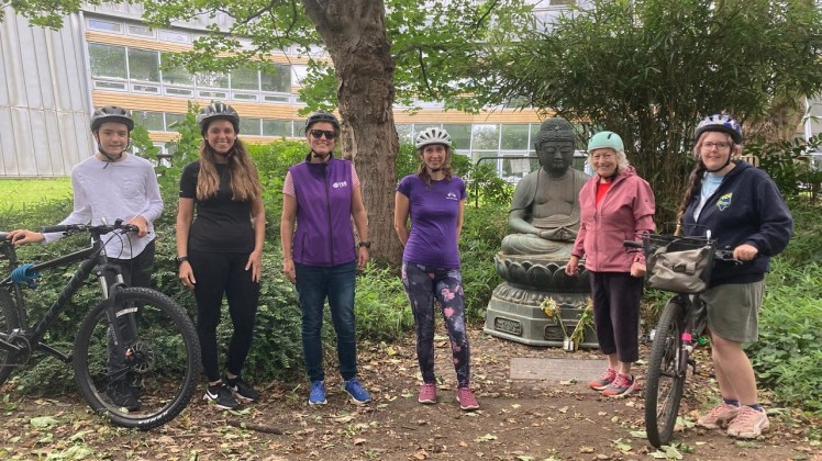 People in bike helmets by a Buddha under sycamore tree