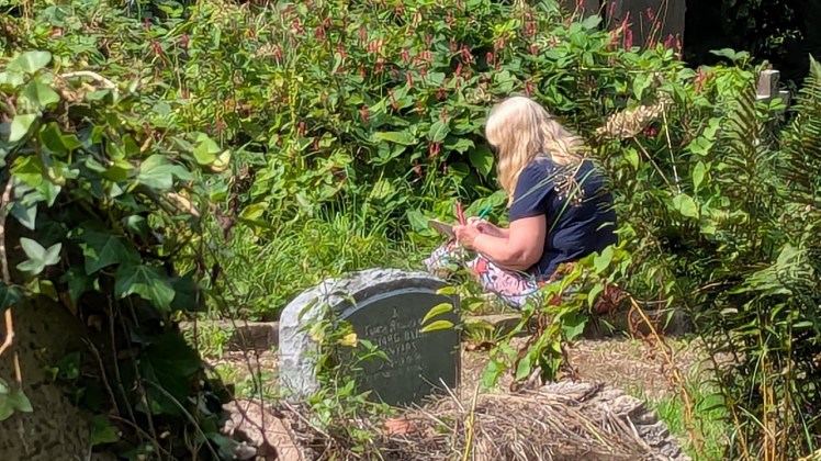 Woman sitting drawing amongst the flowers at York Cemetery