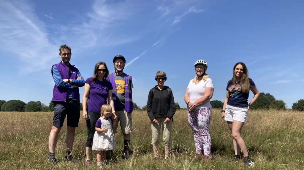 Group stand together on Hob Moor under a blue sky. Some wear cycling helmets.
