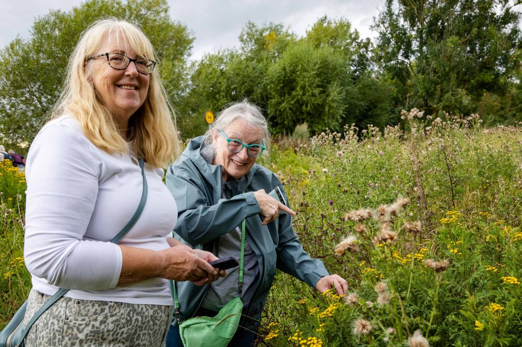 Two women smile and look at wildflowers